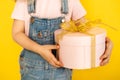 in the hands of a little girl, a gift in a pink round box with a golden bow, on a yellow background Royalty Free Stock Photo