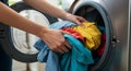 Hands loading colorful clothes into a front-loading washing machine. The Royalty Free Stock Photo
