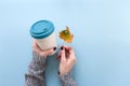 Hands in long sleeve knitted sweater, holding bamboo reusable cup and autumn leaf, overhead on blue background Royalty Free Stock Photo