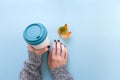 Hands in long sleeve knitted sweater, holding bamboo reusable cup and autumn leaf, overhead on blue background Royalty Free Stock Photo