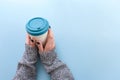 Hands in long sleeve knitted sweater, holding bamboo reusable cup with lid on, overhead on blue background Royalty Free Stock Photo