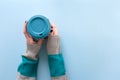 Hands in long sleeve knitted sweater, holding bamboo reusable cup with lid on, overhead on blue background Royalty Free Stock Photo