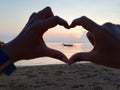 Hands love sign against sunset colors over the sea background.