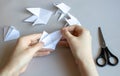 Hands make white paper fish on a gray table.There are scissors next to it