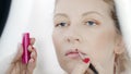 Hands of makeup artist apply lipstick with brush on lips, makeup the face of a caucasian blonde woman with blue eyes, close up Royalty Free Stock Photo