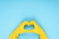 hands making heart shape with yellow cleaning glove on blue background Royalty Free Stock Photo