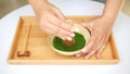 Hands making Japanese organic matcha green tea ceremony by bamboo whisk chasen on wood tray