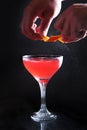 The hands of a male bartender spraying orange peel juice on a cocktail on a dark background. Close-up of the hands