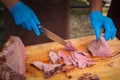 Hands of a male chef in blue gloves cutting a piece of grilled beef
