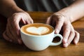 Hands of a man or barista holding cup of hot coffee latte with heart shaped foam art Royalty Free Stock Photo