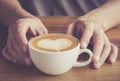 Hands of a man or barista holding cup of hot coffee latte with heart shaped foam art Royalty Free Stock Photo