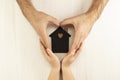 Hands of a man and a child surround a model of a dark house on a gray background. Family, real estate and insurance concept, flat