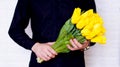 A man in a black shirt holds a bouquet of yellow tulips on a white background Royalty Free Stock Photo