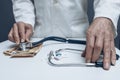 hands of man dressed in white doctor's coat picking up stethoscope located with pile of fifty euro bills and bunch of pills