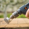 Hands man with electrical rotating brush metal disk sanding a piece of wood