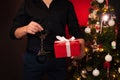 hands of a man with a gift box and BDSM handcuffs at the Christmas tree. Erotic gift for the new year for sexual games Royalty Free Stock Photo