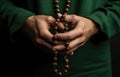 Hands of a man in a green cassock holding a rosary beads