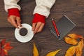 Hands of man hold a cup of coffee at wooden table with notebook and pen and autumn leaves Royalty Free Stock Photo