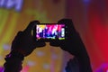 Hands of a man holding a smartphone filming the scene at a music festival