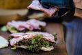 Hands of a man preparing a fresh healthy sandwich or burger with ham, green salad on a brown wooden table at a street food market, Royalty Free Stock Photo