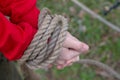 The hands of a man in a red jacket tied with a thick rope outdoors Royalty Free Stock Photo