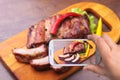 Hands of man with smartphone taking photo grilled barbecued ribs with lettuce leaves, hot chili pepper and sauce on