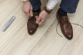 Hands of man in suit pants tying laces on classic shoes in everyday lifestyle