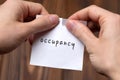 Hands of a man tearing a piece of paper with inscription occupancy