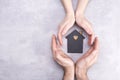 Hands of man and woman surround a model of a dark house on a gray background. Real estate and insurance concept, flat lay, top