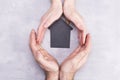 Hands of man and woman surround a model of a dark house on a gray background. Real estate and insurance concept, flat lay, top