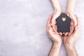 Hands of man and woman surround a model of a dark house on a gray background. Real estate and insurance concept, flat lay, top