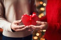The hands of a man and a woman in sweaters hold a red gift box in the shape of a heart. Celebrating Valentine\'s Day Royalty Free Stock Photo