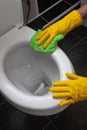 Hands of man in yellow gloves cleaning toilet bowl using cloth and detergent, concept for house cleaning and household duties Royalty Free Stock Photo