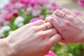 Hands of married couple with wedding rings against pink flowers