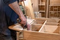 hands of a master carpenter install the hinges on the cabinet with a hand-held power tool screwdriver. Production of handmade