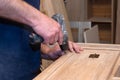 hands of a master carpenter install the hinges on the cabinet with a hand-held power tool screwdriver. Production of handmade