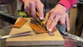 Hands of master measure leather with tool, trim for further work with knife. Shoemaker workplace