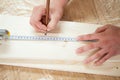 Hands measuring wooden plank with measuring tape and pencil