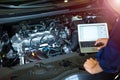 Mechanic Using Laptop While Examining Car Engine