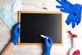 Hands in medical gloves write in chalk on a blackboard surrounded by gloves, medical face mask, antiseptic and thermometer on