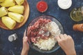 Hands mixing minced meat, chopped onion, boiled rice and seasons in the big glass bowl.