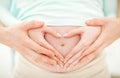 Hands of Mom and Dad on the pregnant belly in shape of heart on Royalty Free Stock Photo