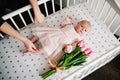 Hands of the mother who takes gift on a holiday. Newborn baby girl with bouquet of flowers pink tulips on a bed. Royalty Free Stock Photo