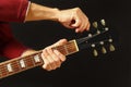 Hands of musician tunes the guitar on dark background