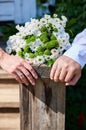 Hands of newly married couple next to wedding bouquet of white decorative daisy lying on natural old wooden plank Royalty Free Stock Photo