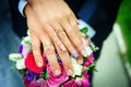 Hands of newlyweds on the background of wedding bouquet. Gold wedding rings on the finger of bride and groom, close-up. Concept