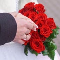 Hands of newlyweds with a red roses bouquet.