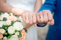 Hands of the newlyweds bride and groom with gold wedding rings close-up on a background of a wedding bouquet of roses Royalty Free Stock Photo