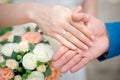 Hands of the newlyweds bride and groom with gold wedding rings close-up on a background of a wedding bouquet of roses Royalty Free Stock Photo