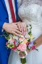 Hands of newlyweds with wedding rings and a bouquet of flowers. The groom in a blue suit and red tie. The concept of Royalty Free Stock Photo